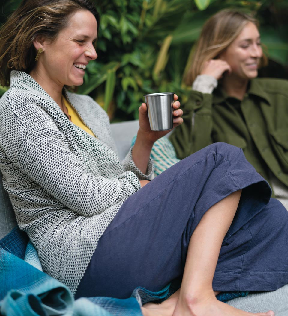 Woman sat down holding a Klean Kanteen plastic-free steel cup in front of a green background