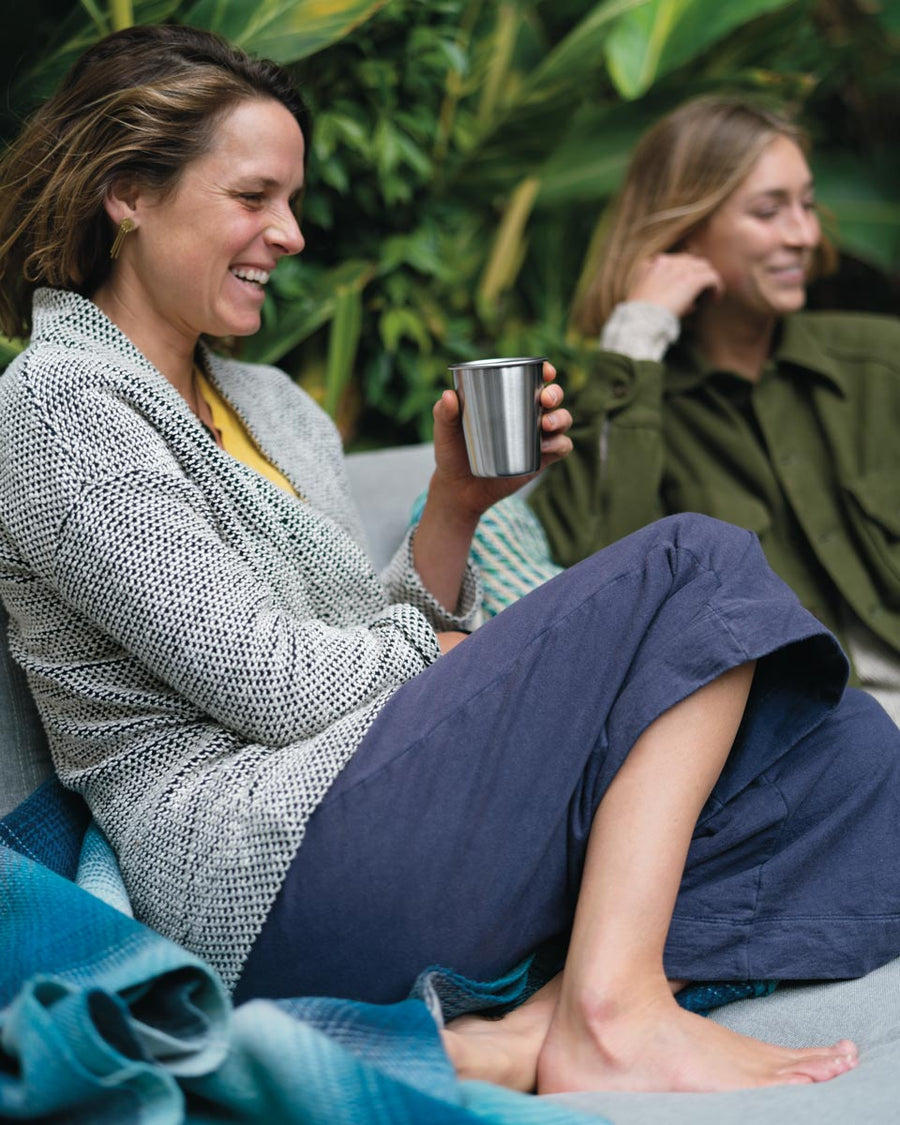 Woman sat down holding a Klean Kanteen plastic-free steel cup in front of a green background