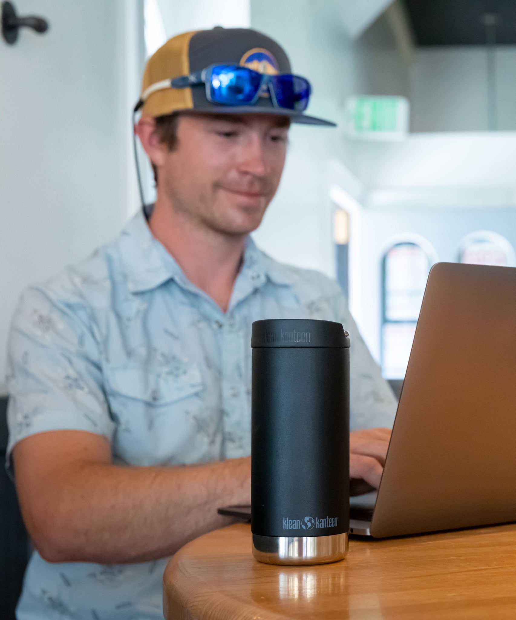 A person sitting at atable in front of a laptop with Klean Kanteen 12oz TKWide Cafe in the black colour placed in front of them.