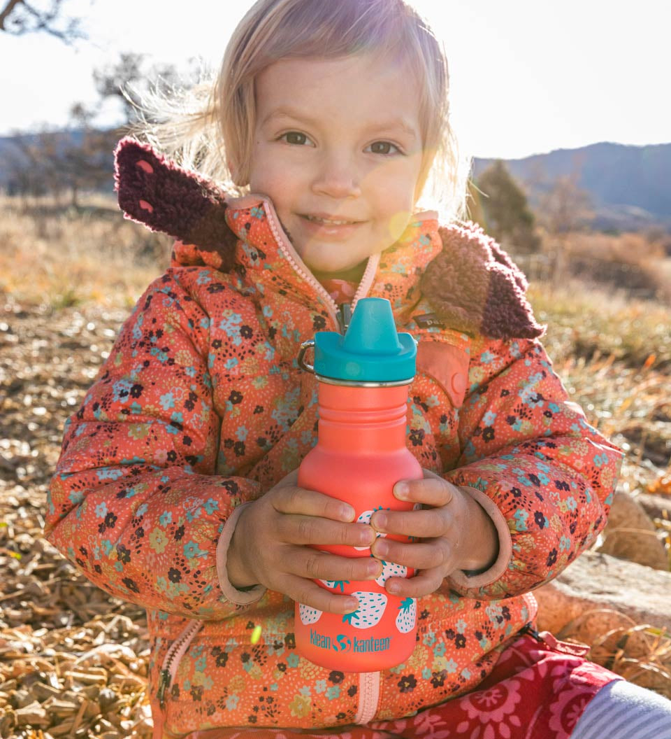 Girl sat on some rocks holding a Klean Kanteen 12oz kids sippy drinks bottle 