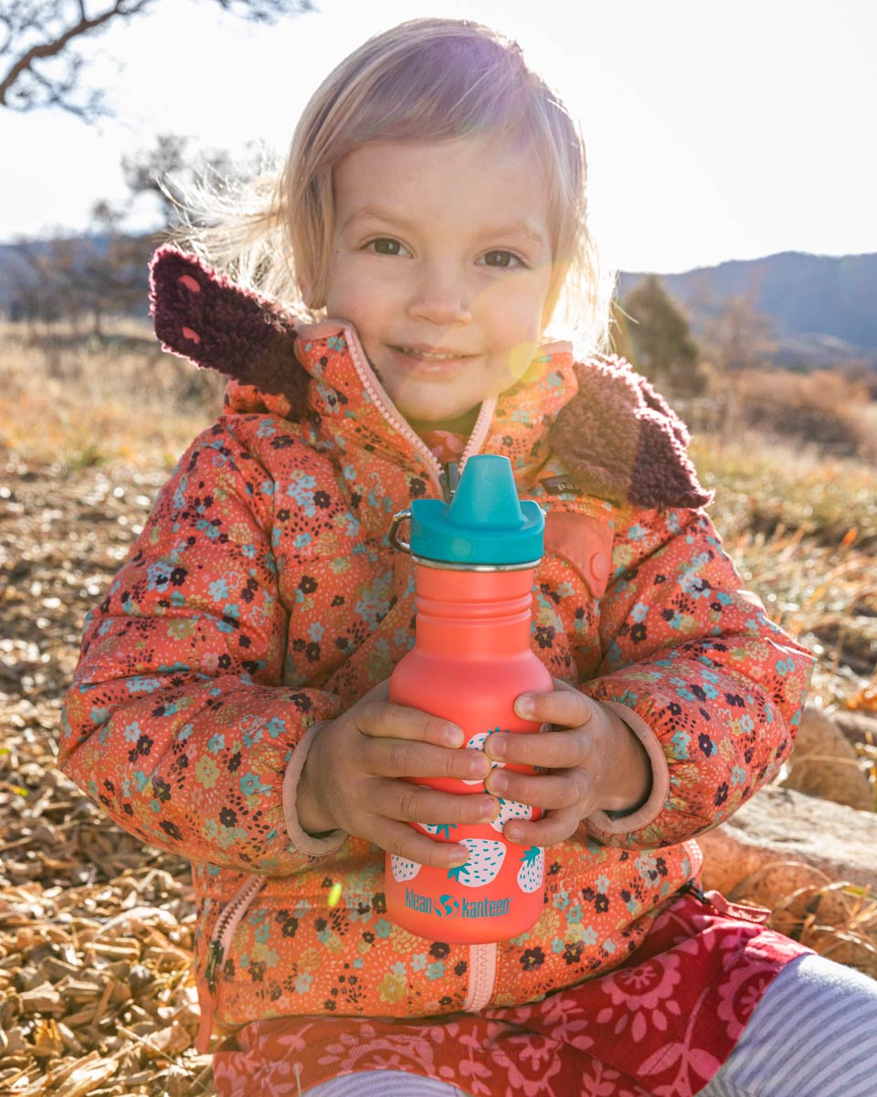 Girl sat on some rocks holding a Klean Kanteen 12oz kids sippy drinks bottle 