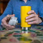 A close up of a person's hand holding the Klean Kanteen 12oz TKWide Cafe in the sunset colour with the taupe coloured lid in their other hand. 