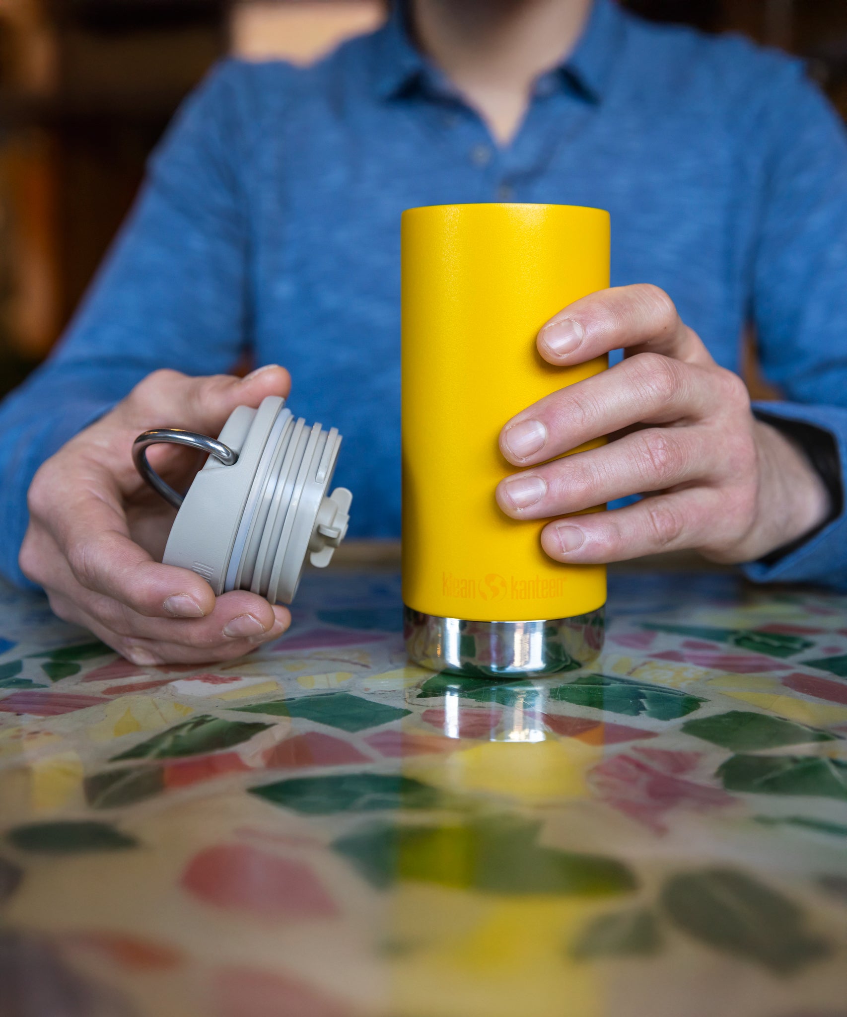 A close up of a person's hand holding the Klean Kanteen 12oz TKWide Cafe in the sunset colour with the taupe coloured lid in their other hand. 