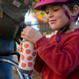 A child holding a Klean Kanteen 12oz Tofu Strawberries Print TKWide. The child is wearing a bike helmet. 