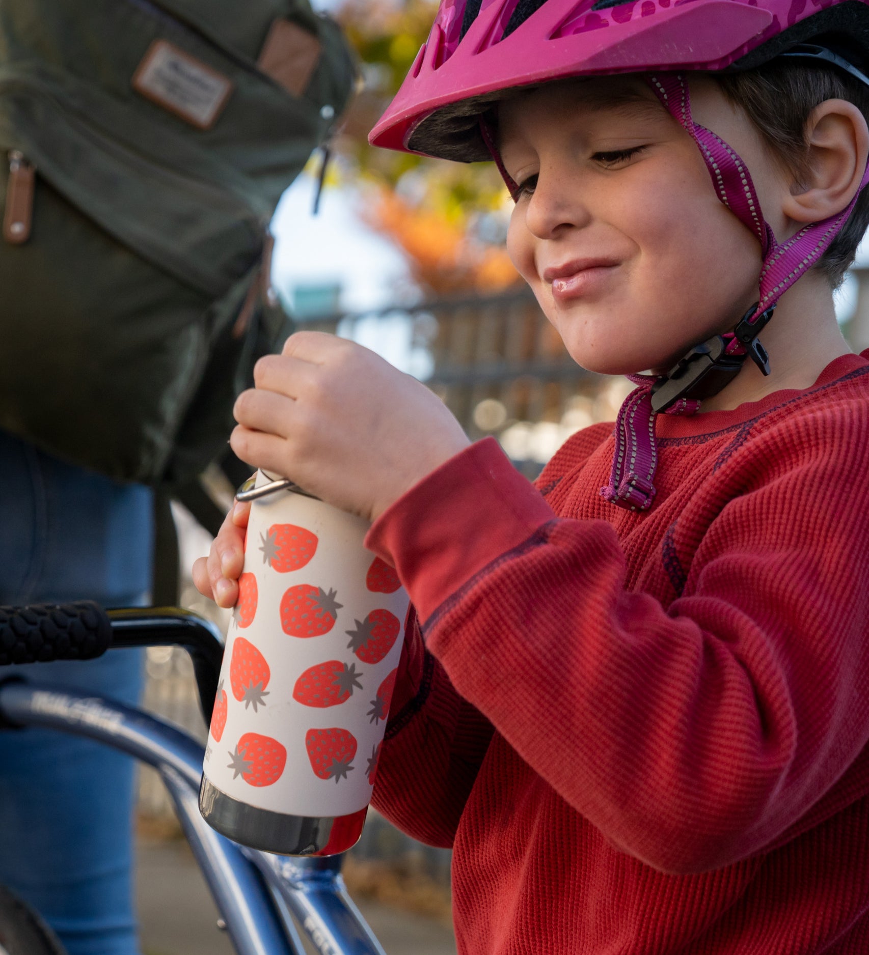 A child holding a Klean Kanteen 12oz Tofu Strawberries Print TKWide. The child is wearing a bike helmet. 