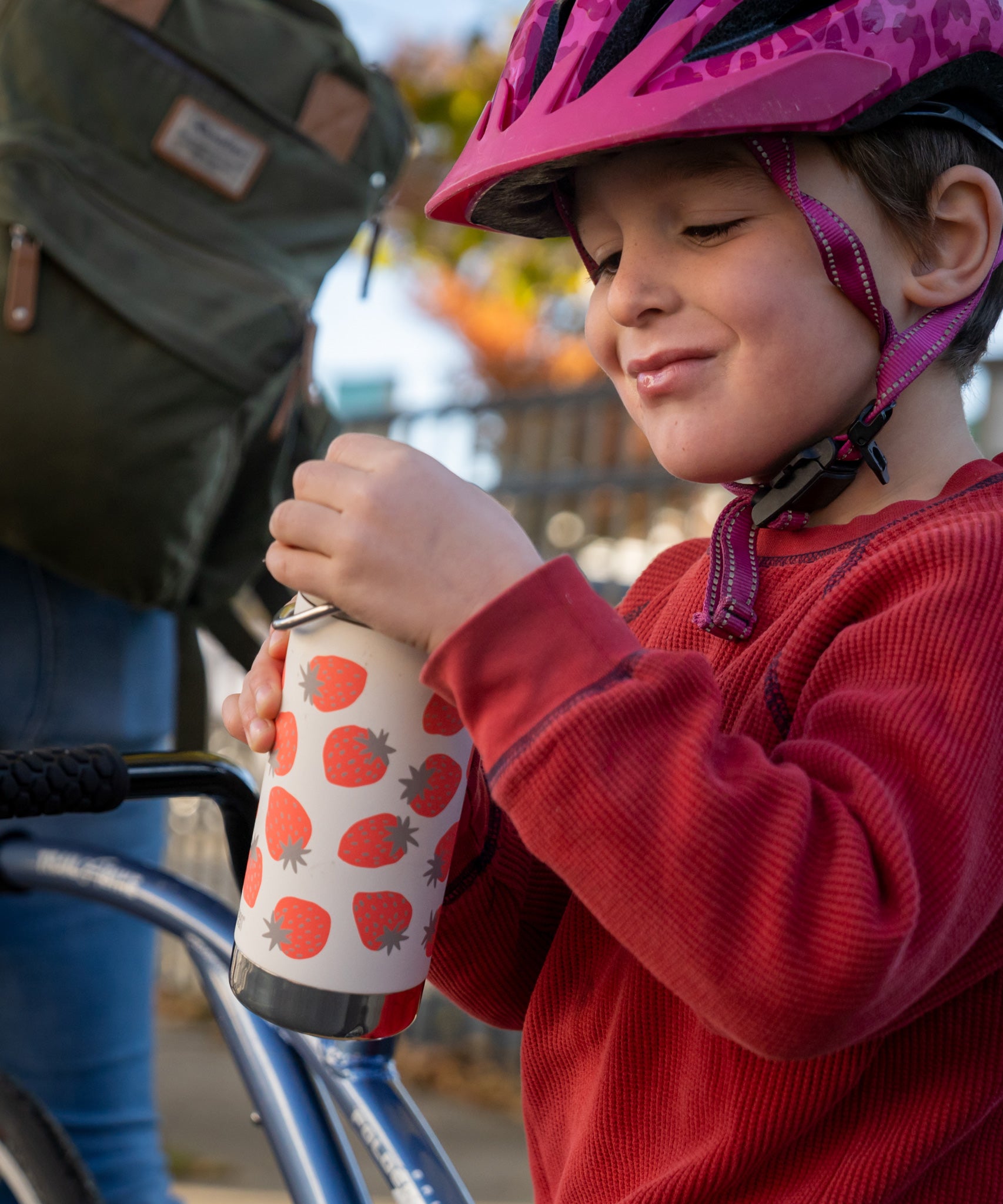 A child holding a Klean Kanteen 12oz Tofu Strawberries Print TKWide. The child is wearing a bike helmet. 