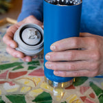 A close up of a person with a Klean Kanteen 16oz TKWide in blue colour in their hand with taupe Cafe cap. 