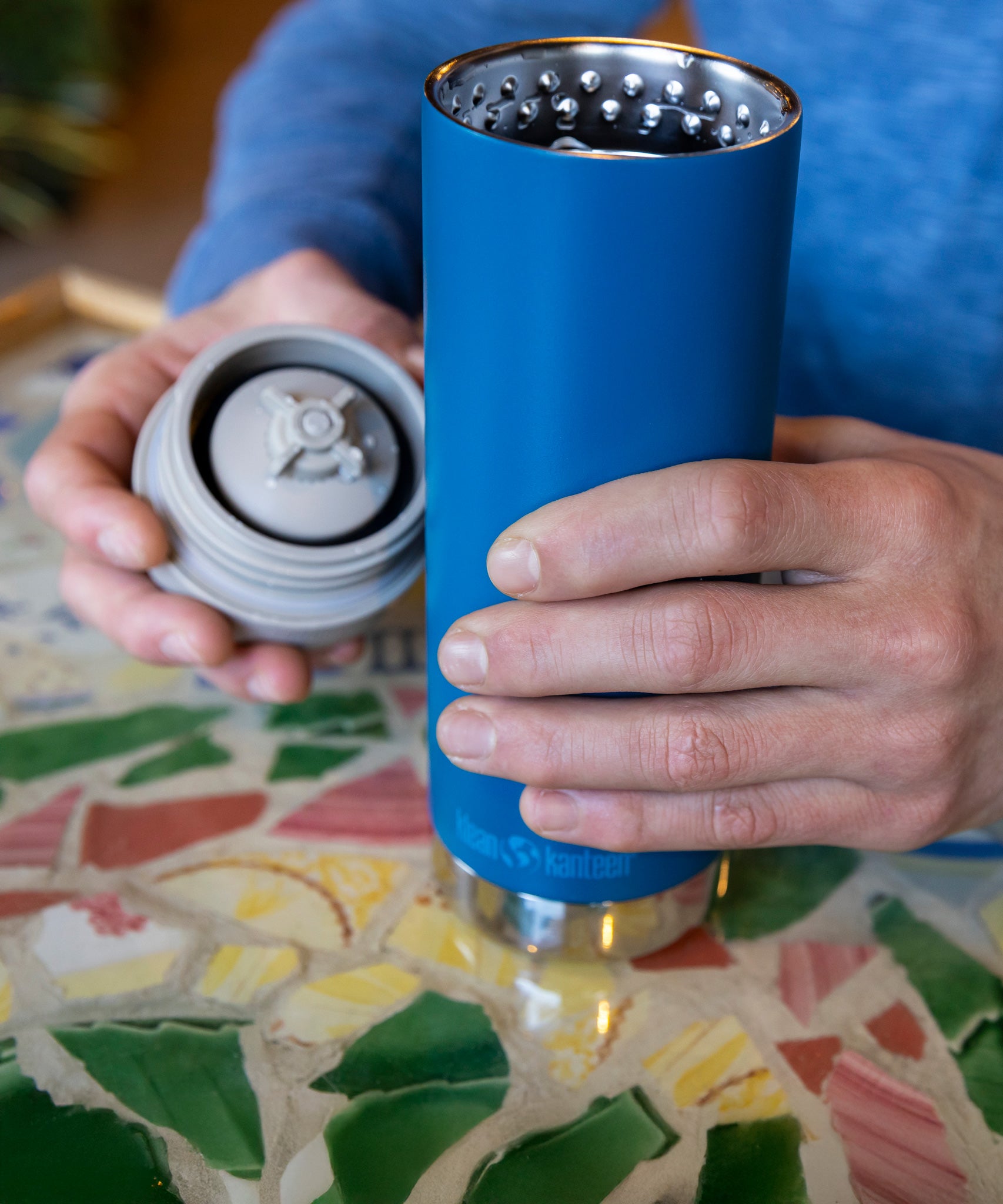 A close up of a person with a Klean Kanteen 16oz TKWide in blue colour in their hand with taupe Cafe cap. 