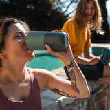 Close up of woman drinking from a Klean Kanteen stainless steel drinks tumbler next to a stone wall