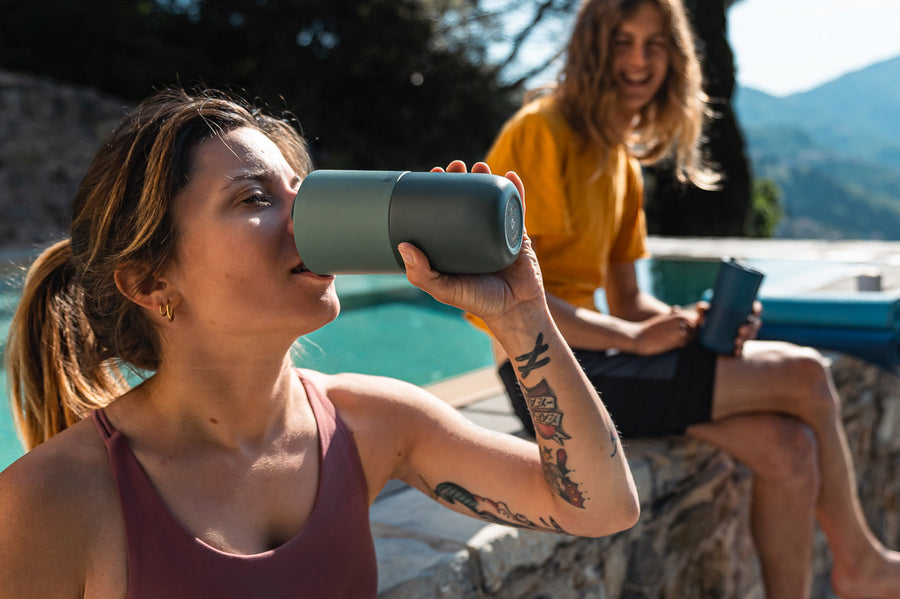 Close up of woman drinking from a Klean Kanteen stainless steel drinks tumbler next to a stone wall