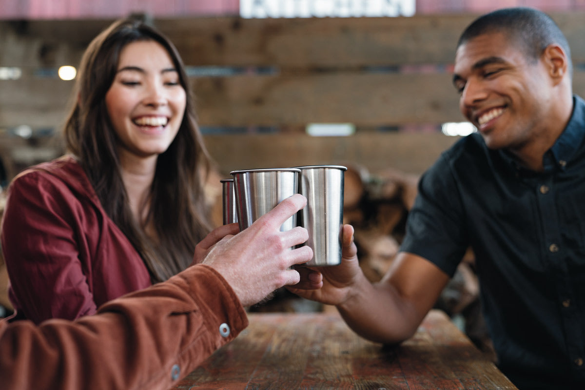 3 people holding up Klean Kanteen 16oz stainless steel cups together in the middle of a table