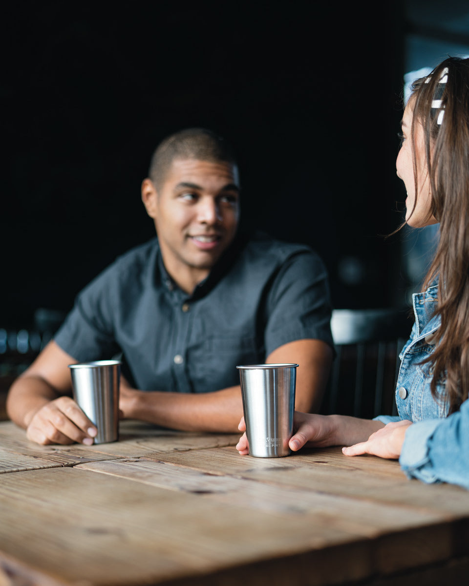 Close up of man and woman sat at a wooden table with some Klean kanteen eco-friendly stainless steel cups