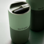 Close up of a Klean Kanteen 16oz insulated tumbler with its lid open on a dark green background