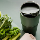 Close up of the flip lid on the Klean Kanteen stainless steel insulated drinks tumbler on a dark green background next to an apple