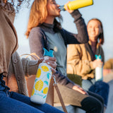 Close up of woman holding the Klean Kanteen 27oz lemon sports bottle next to a woman drinking from a klean kanteen metal bottle