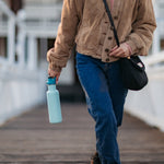 Close up of lady walking and carrying the Klean Kanteen 27oz narrow metal water bottle on a wooden path