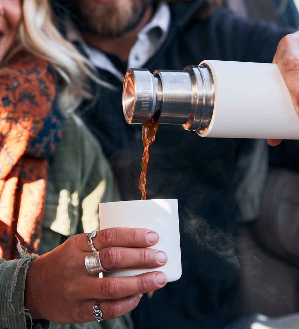 Close up of a man and woman pouring some liquid into the cup of a Klean kanteen 500ml tkpro insulated flask