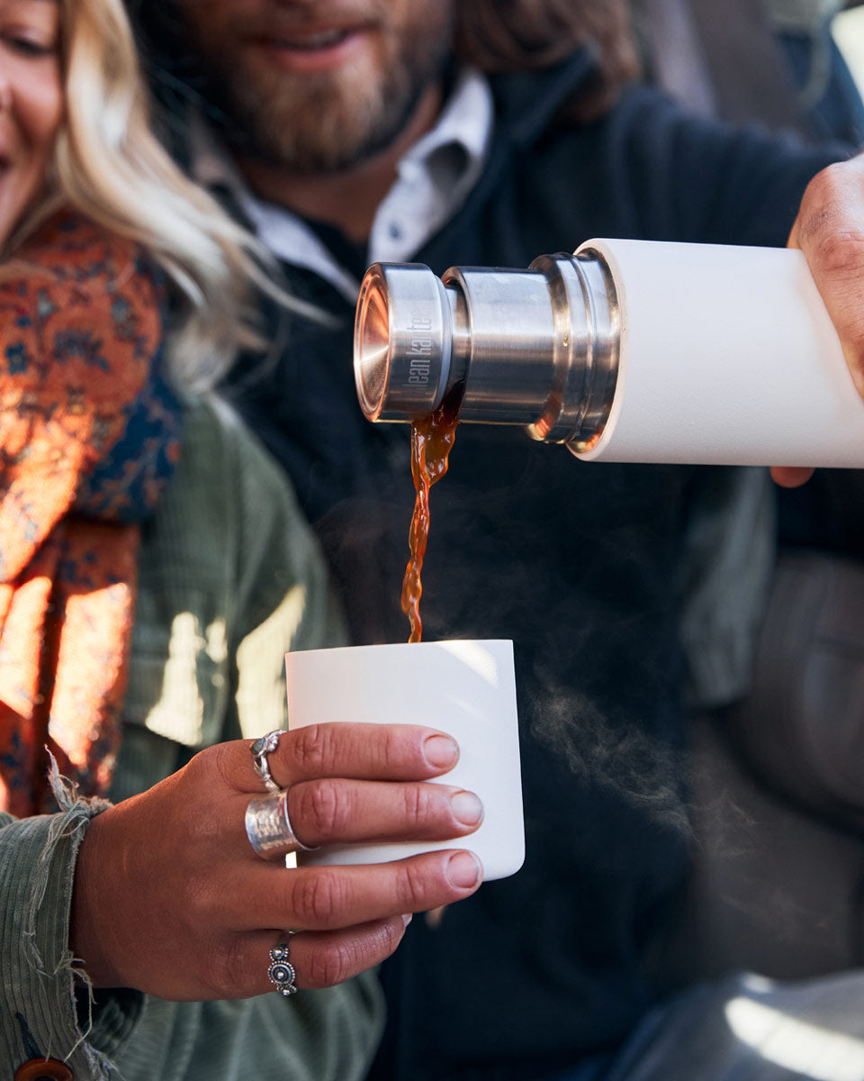 Close up of a man and woman pouring some liquid into the cup of a Klean kanteen 500ml tkpro insulated flask