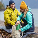 Man and woman sat on a log putting a Klean kanteen 750 ml steel tkpro flask into the side pocket of a rucksack