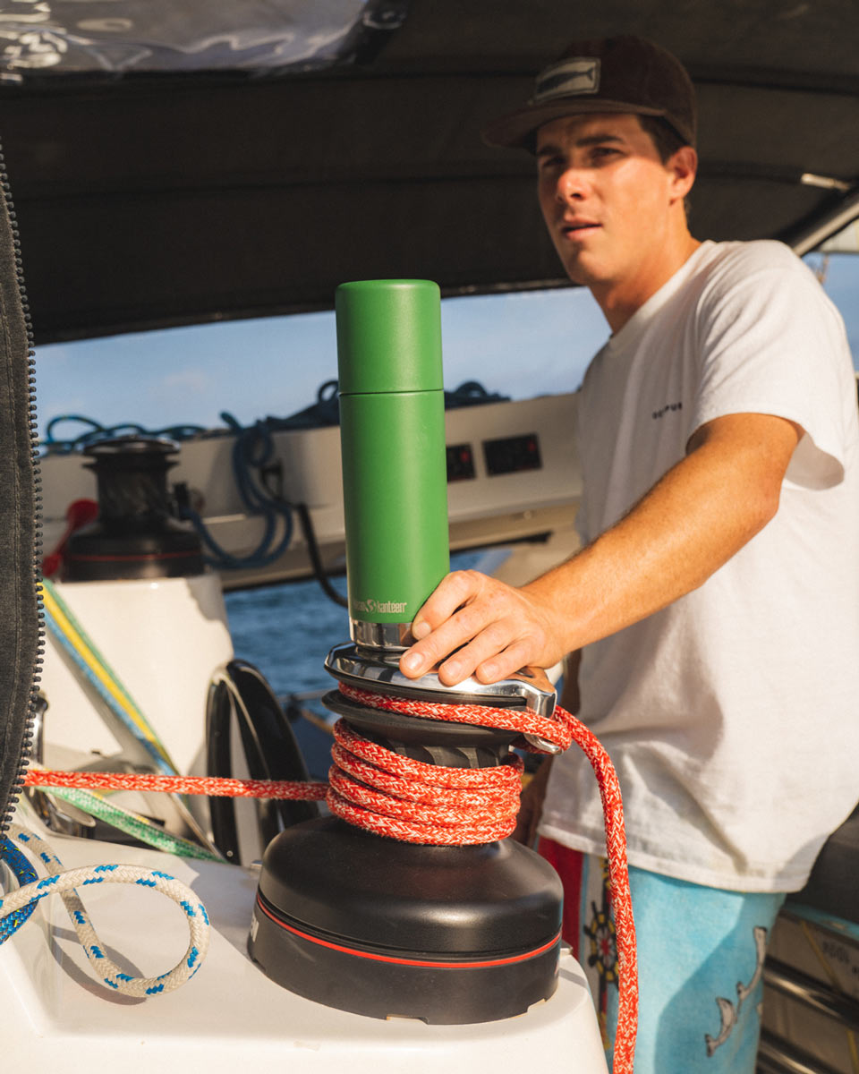 Man stood driving a boat and holding onto a Klean kanteen reusable stainless steel tkpro flask