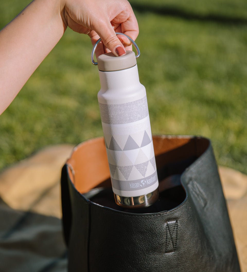 Close up of womans hand pulling a Klean Kanteen stainless steel insulated bottle from a handbag