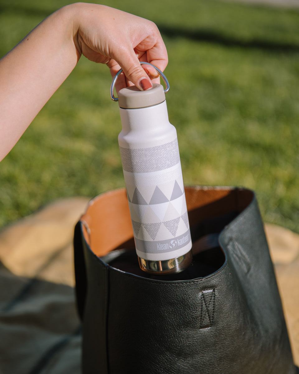 Close up of womans hand pulling a Klean Kanteen stainless steel insulated bottle from a handbag