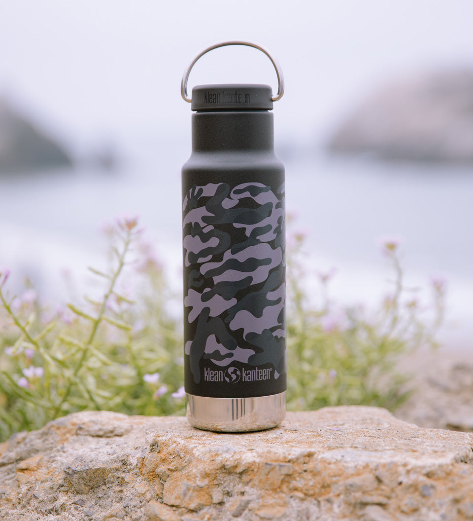 Close up of a Klean Kanteen 12oz insulated classic bottle in the black camo print on a stone wall