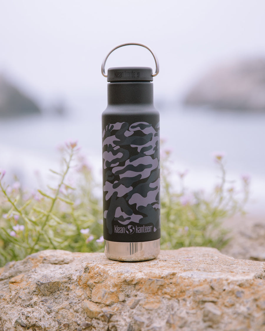 Close up of a Klean Kanteen 12oz insulated classic bottle in the black camo print on a stone wall