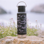 Close up of a Klean Kanteen 12oz insulated classic bottle in the black camo print on a stone wall