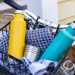 2 klean kanteen classic insulated pour through bottles in a bike basket next to some steel cups