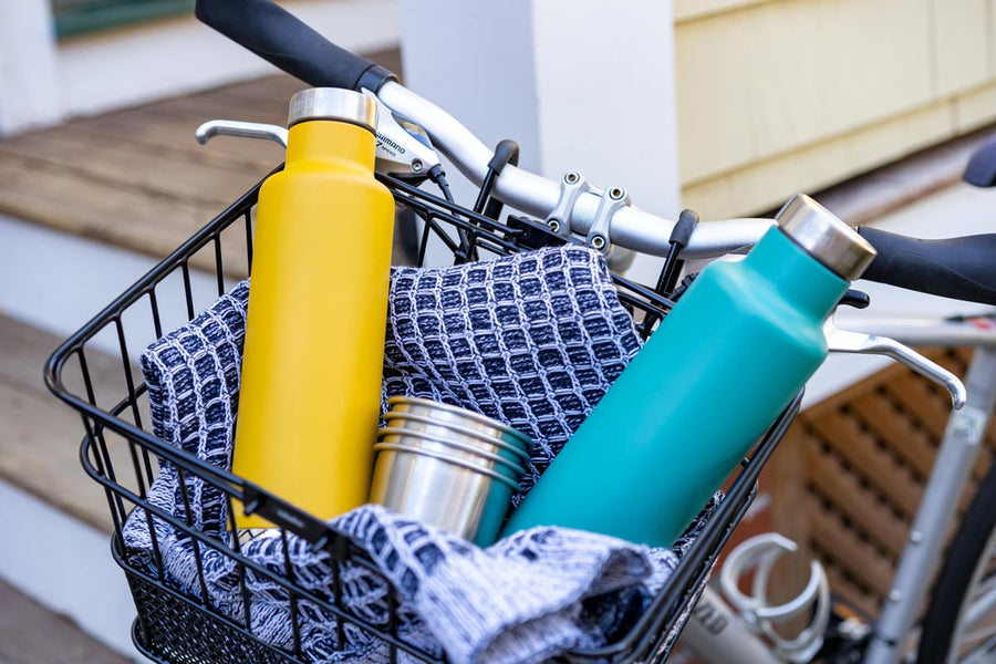 2 klean kanteen classic insulated pour through bottles in a bike basket next to some steel cups