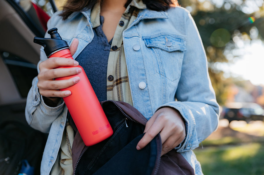 Close up of a woman putting a Klean Kanteen single wall steel bottle with a sports lid into a rucksack