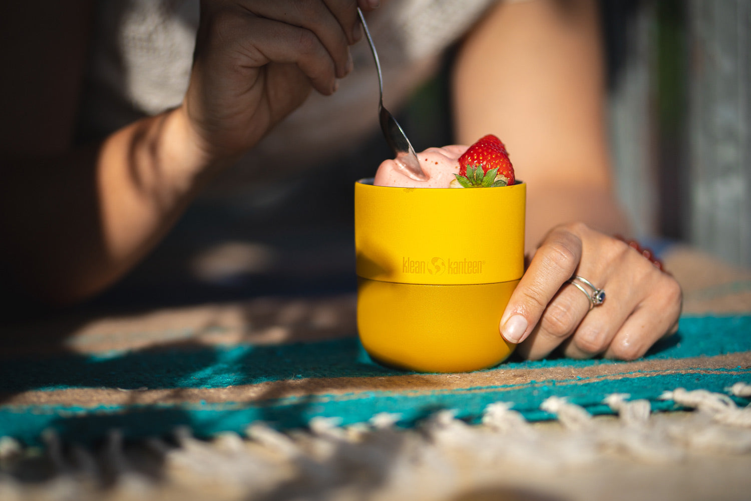 Close up of some hands scooping out some yoghurt from a Klean Kanteen insulated metal lowball glass on a blue blanket