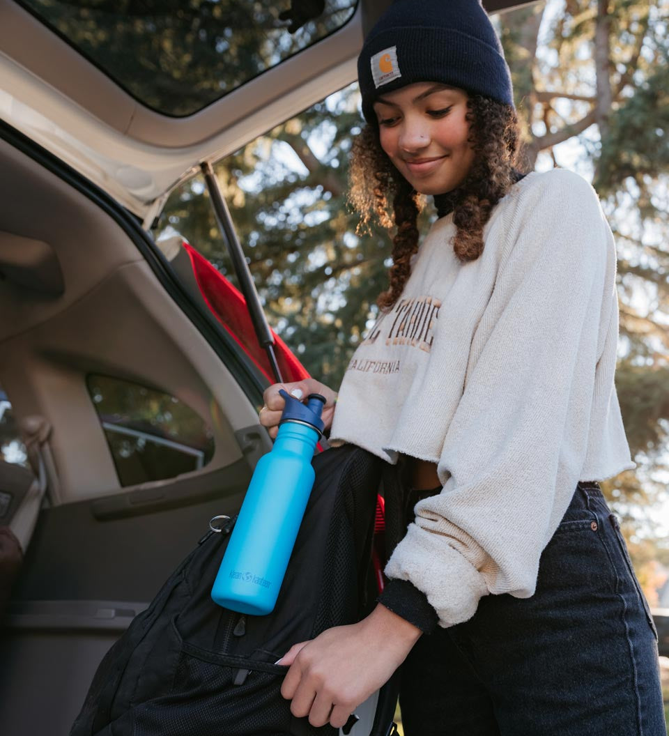 Girl putting the Klean kanteen 18oz reusable metal sports bottle in the side pocket of a backpack