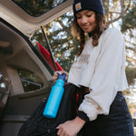 Girl putting the Klean kanteen 18oz reusable metal sports bottle in the side pocket of a backpack