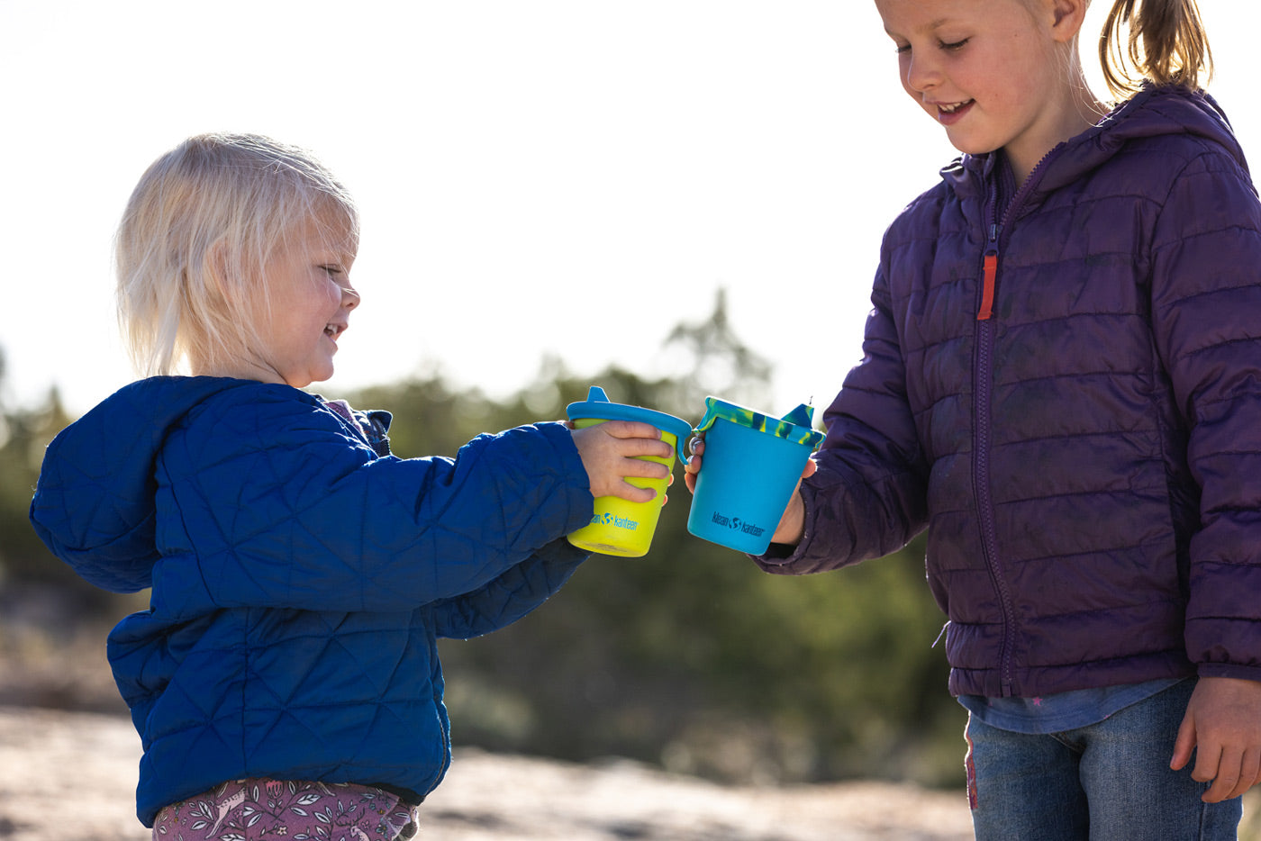 Close up of hands pouring water from a Klean Kanteen TKPro flask into some Kid Kanteen stainless steel drinking cups