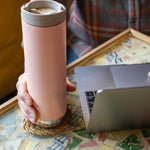 A close up of a person's hand holding onto the peack parfait pink coloured Klean Kanteen 20oz TKWide Cafe.