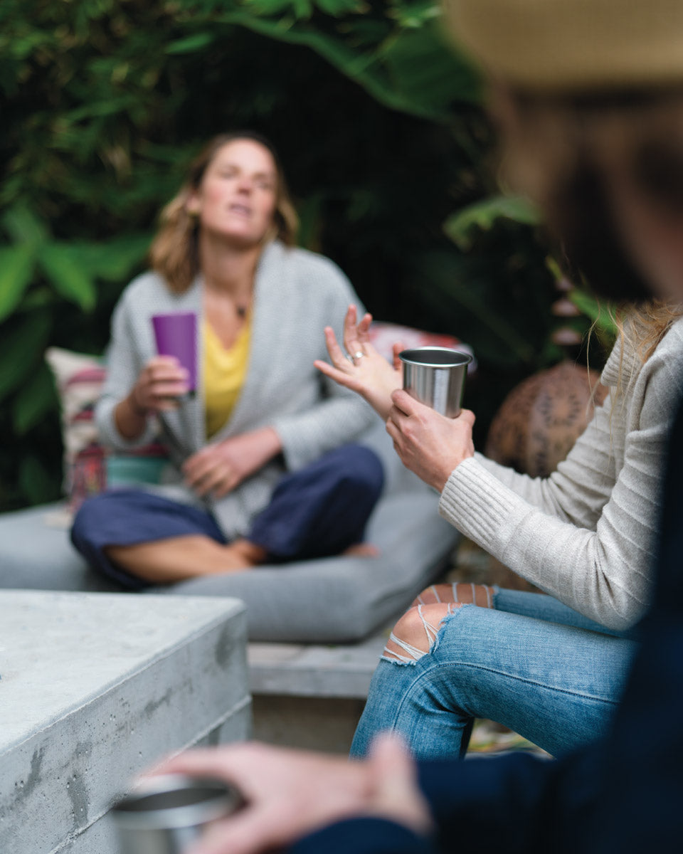 Close up of hand holding the Klean kanteen 10oz stainless steel cup in front of a woman sat on an outdoor seat