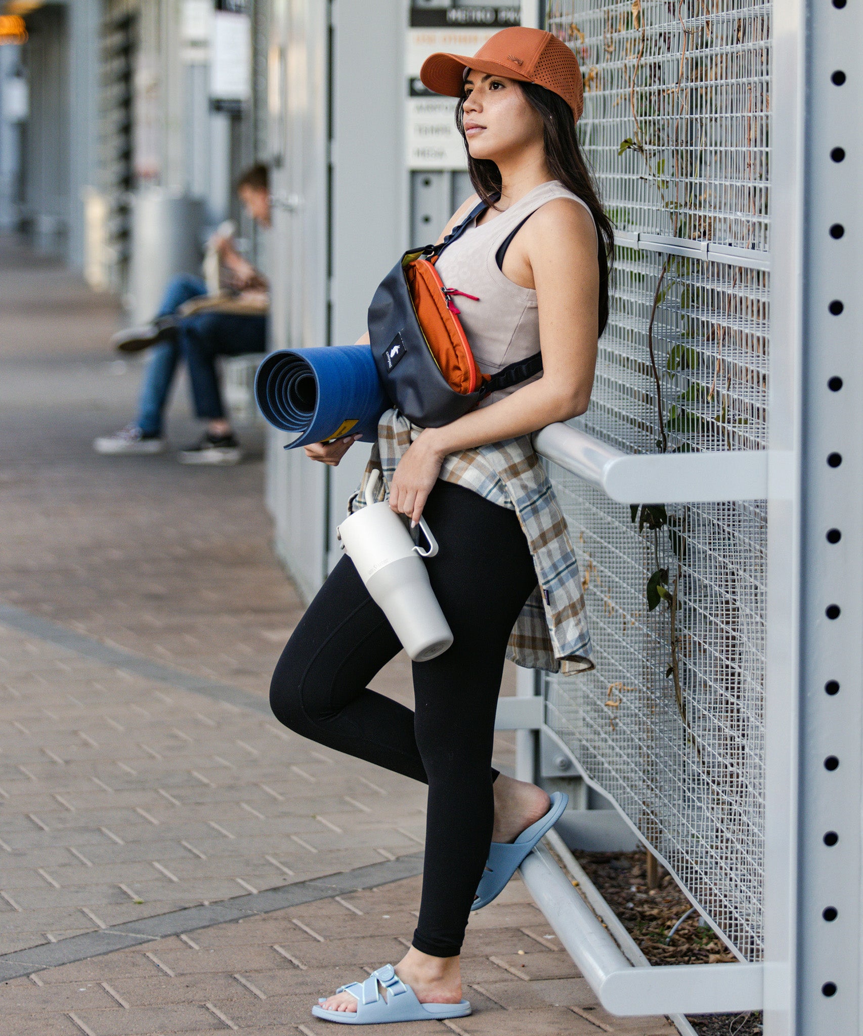 A person is seen leaning against a metal pole with fitness equipment in one hand and a tofu white coloured Klean Kanteen Limited Edition 36oz Rise Tumbler in the other