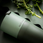 Close up of a Klean Kanteen stainless steel 26oz tumbler on a dark green background next to some green vegetables