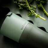 Close up of a Klean Kanteen stainless steel 26oz tumbler on a dark green background next to some green vegetables