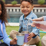 Children holding Klean Kanteen Steel Kid Cups, an adult can be seen pouring raspberry lemonade into the cups. 