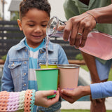 Children holding Klean Kanteen Steel Kid Cups, an adult can be seen pouring raspberry lemonade into the cups. 