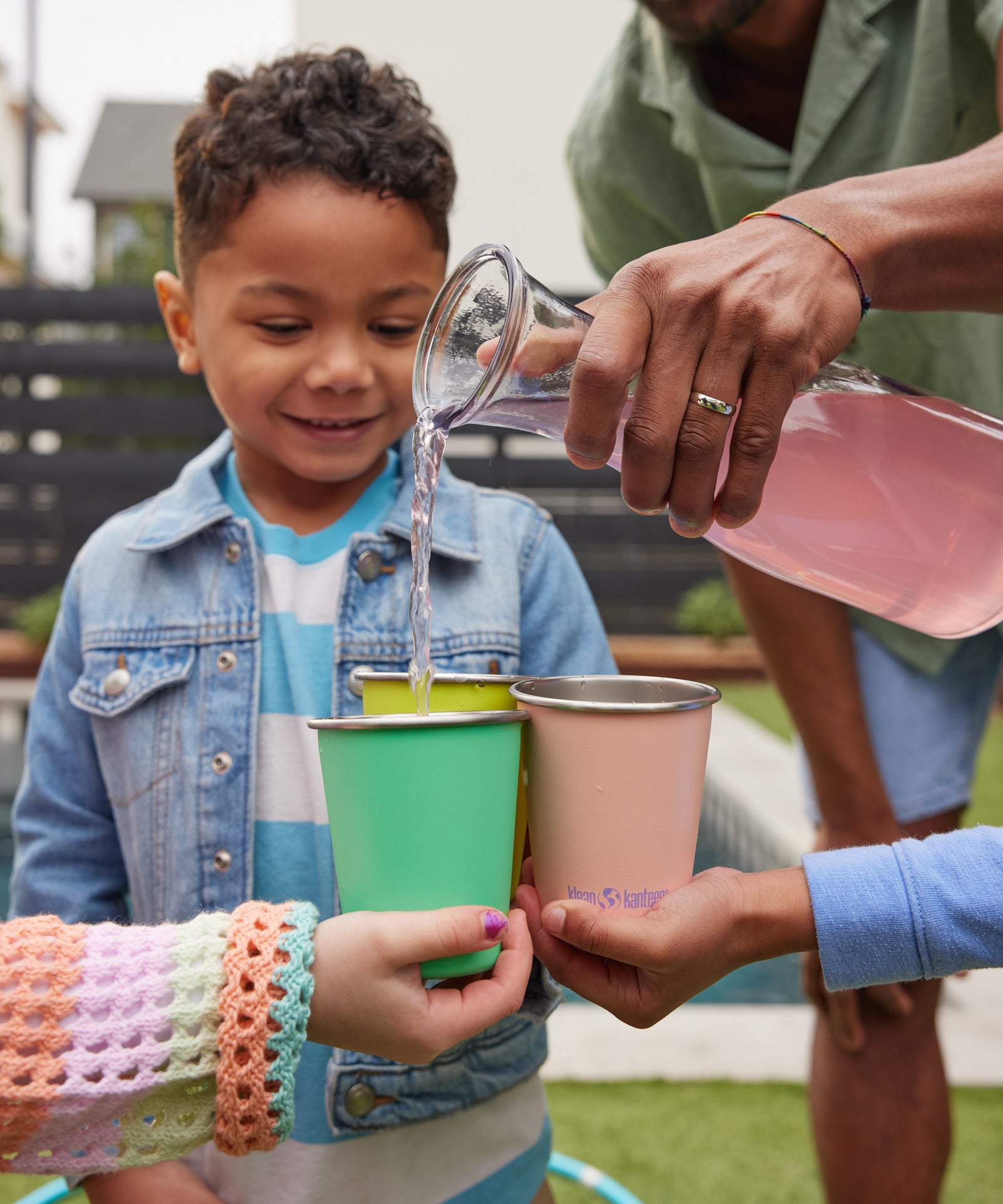 Children holding Klean Kanteen Steel Kid Cups, an adult can be seen pouring raspberry lemonade into the cups. 