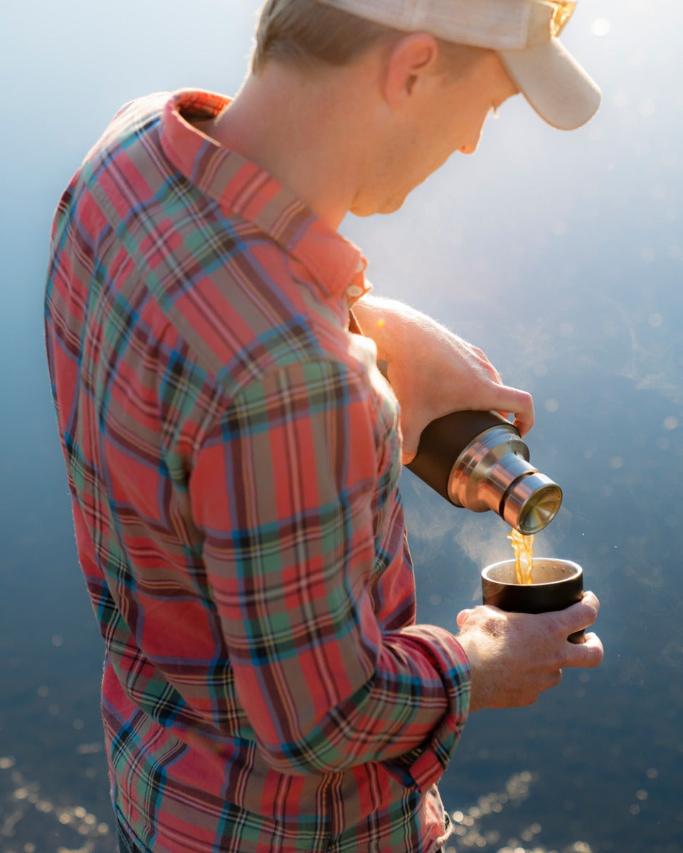 Man crouched down pouring the Klean Kanteen TKPro stainless steel drinks flask next to a stone campfire