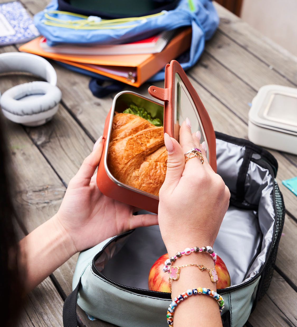 Person opening a Klean Kanteen Rise Stainless Steel Lunch Box with school bags open in the background