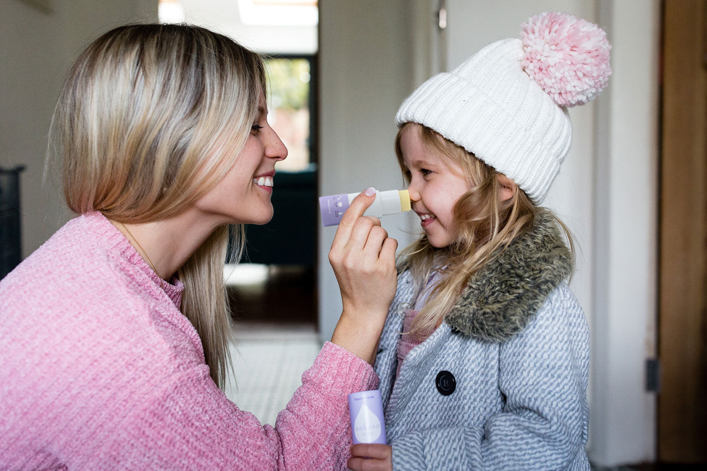 Close up of a woman holding up a Kokoso organic baby balm stick to a child's nose