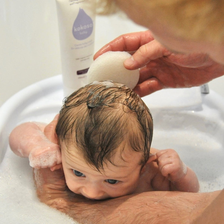 Newborn baby supported by adult in bubbly bath