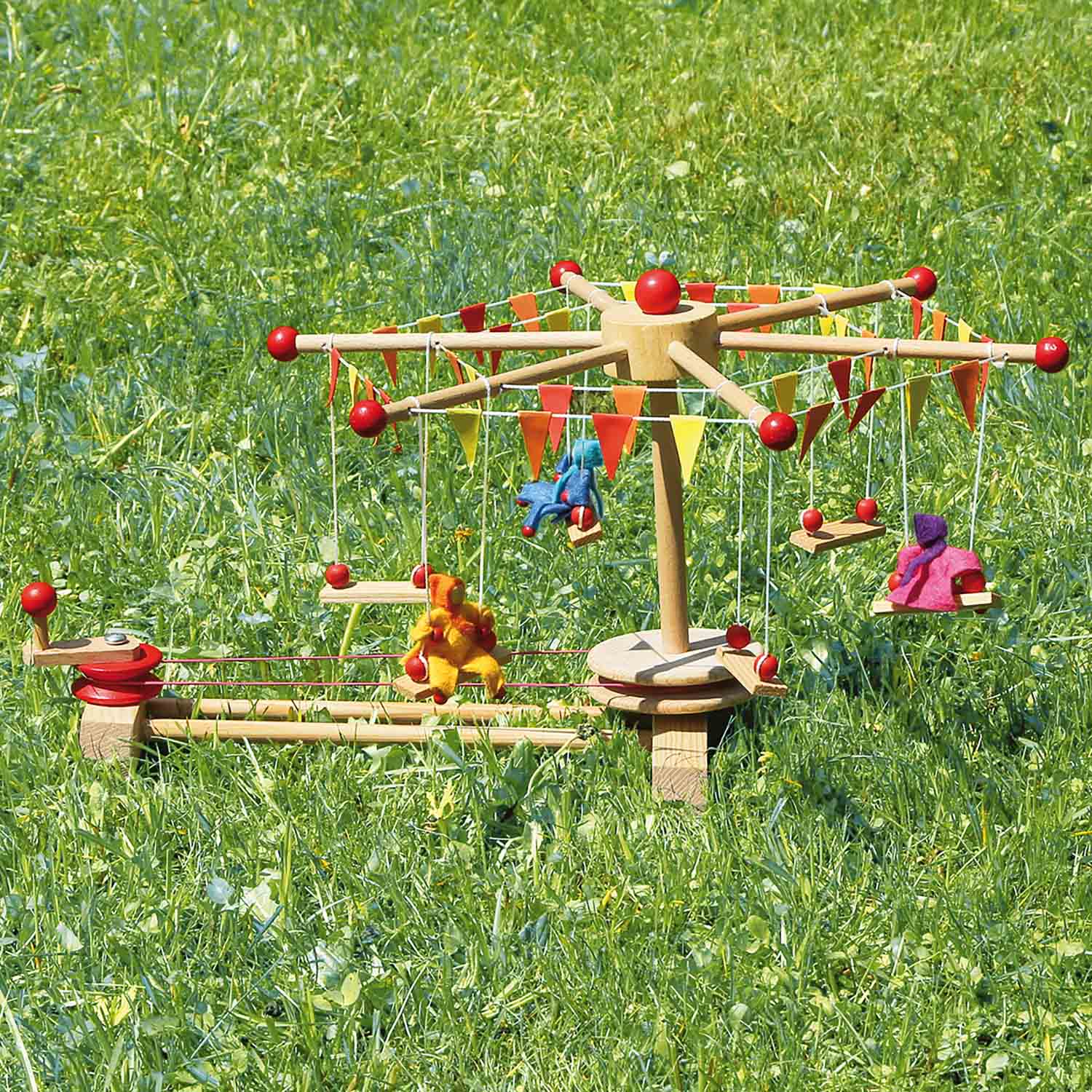 Kraul Wooden Swing Roundabout Kit with passenger dolls outside on the grass