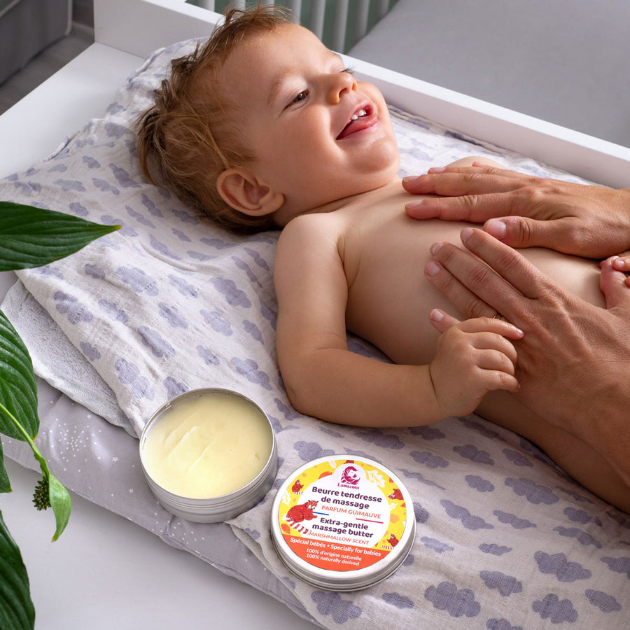 Picture of the Lamazuna Extra Gentle Baby Massage Butter in tin with lid off next to baby